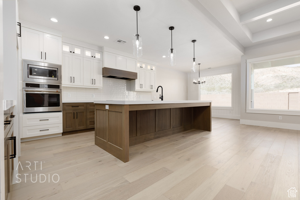 Kitchen featuring stainless steel appliances, light wood-type flooring, an island with sink, and white cabinetry