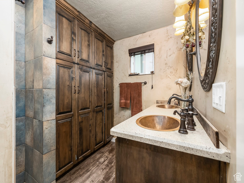 Bathroom with a textured ceiling, dual vanity, and hardwood / wood-style flooring
