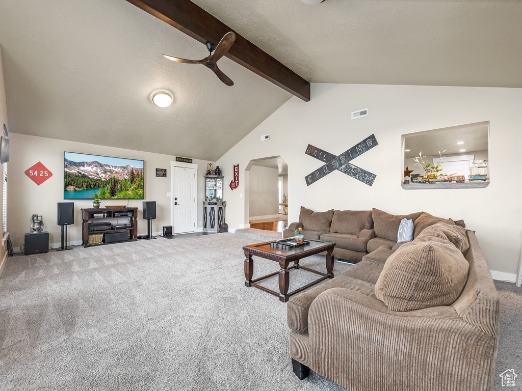 Carpeted living room with high vaulted ceiling, ceiling fan, and beamed ceiling