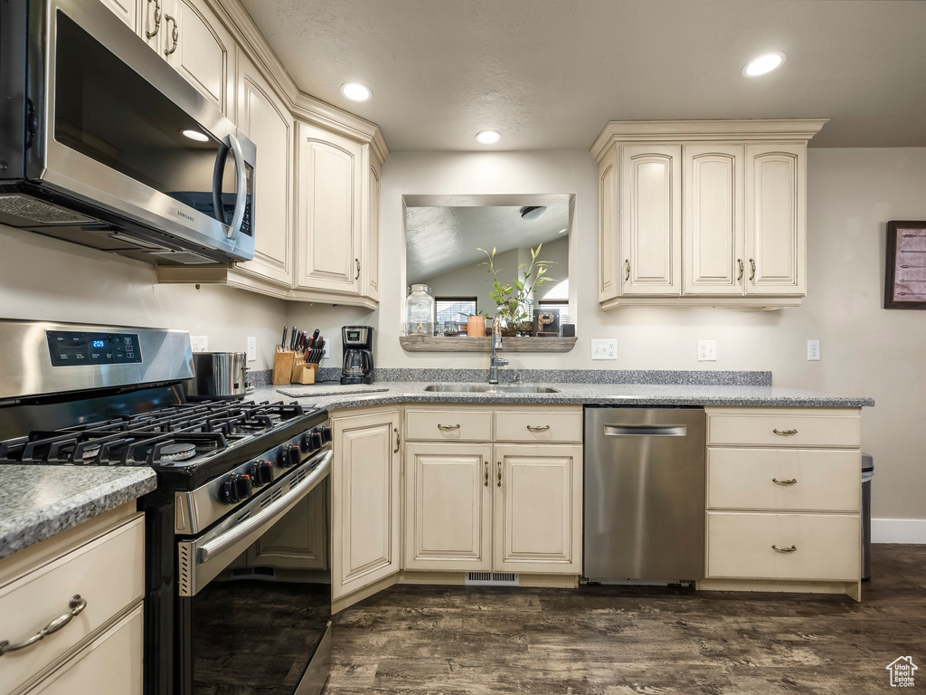 Kitchen with sink, appliances with stainless steel finishes, cream cabinets, and dark hardwood / wood-style flooring