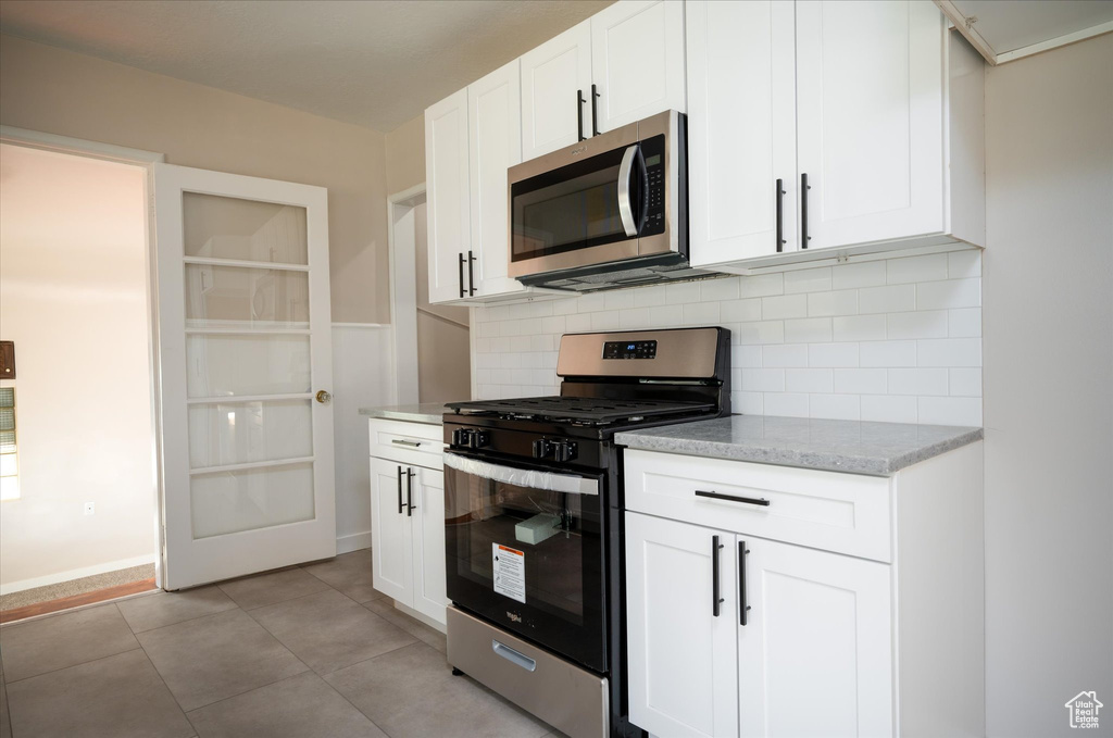 Kitchen with light tile floors, white cabinets, tasteful backsplash, and stainless steel appliances