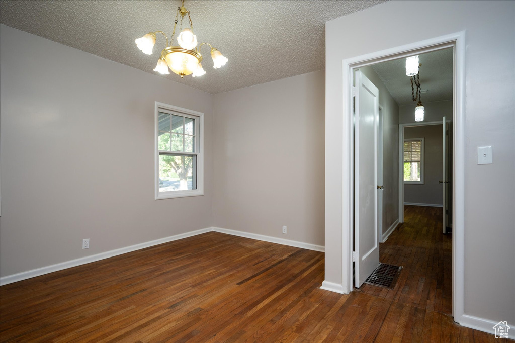 Unfurnished room featuring an inviting chandelier, a textured ceiling, and dark hardwood / wood-style flooring