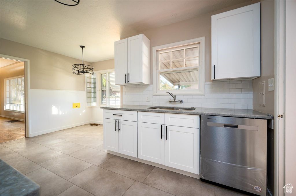 Kitchen with tasteful backsplash, white cabinets, stainless steel dishwasher, pendant lighting, and light tile flooring