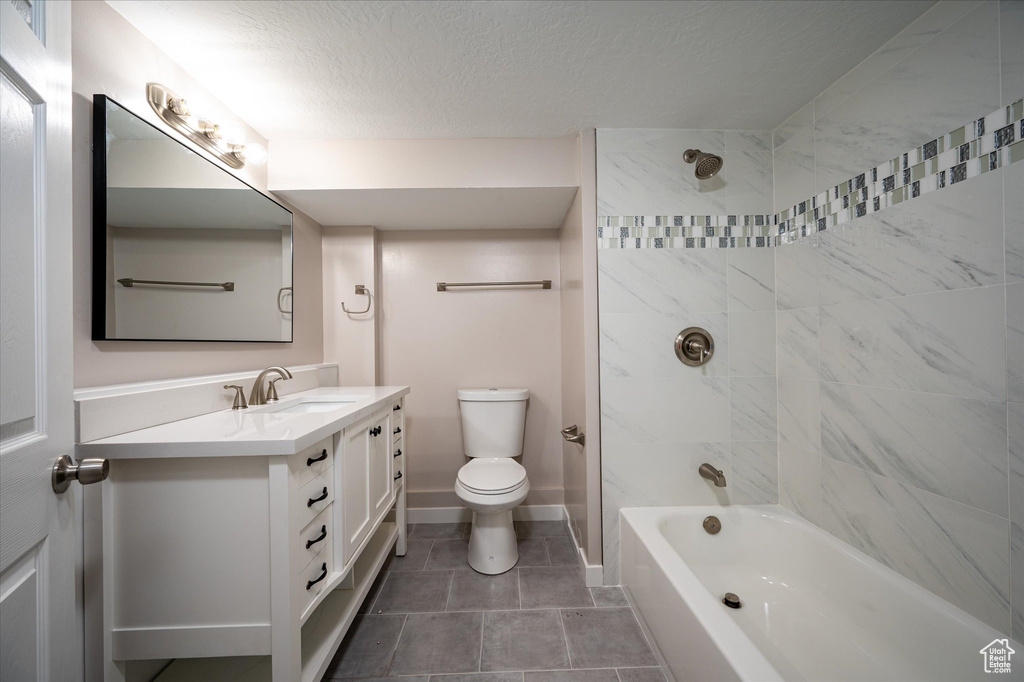 Full bathroom featuring tile flooring, a textured ceiling, toilet, vanity, and tiled shower / bath
