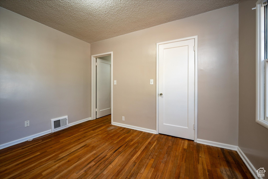 Empty room with a textured ceiling and dark hardwood / wood-style flooring