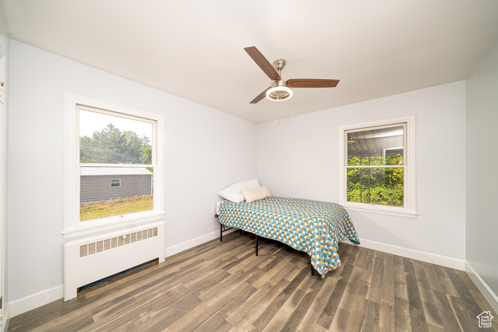 Bedroom with ceiling fan, dark wood-type flooring, and radiator heating unit