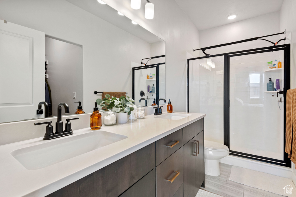 Bathroom featuring a shower with shower door, double sink vanity, toilet, and tile floors