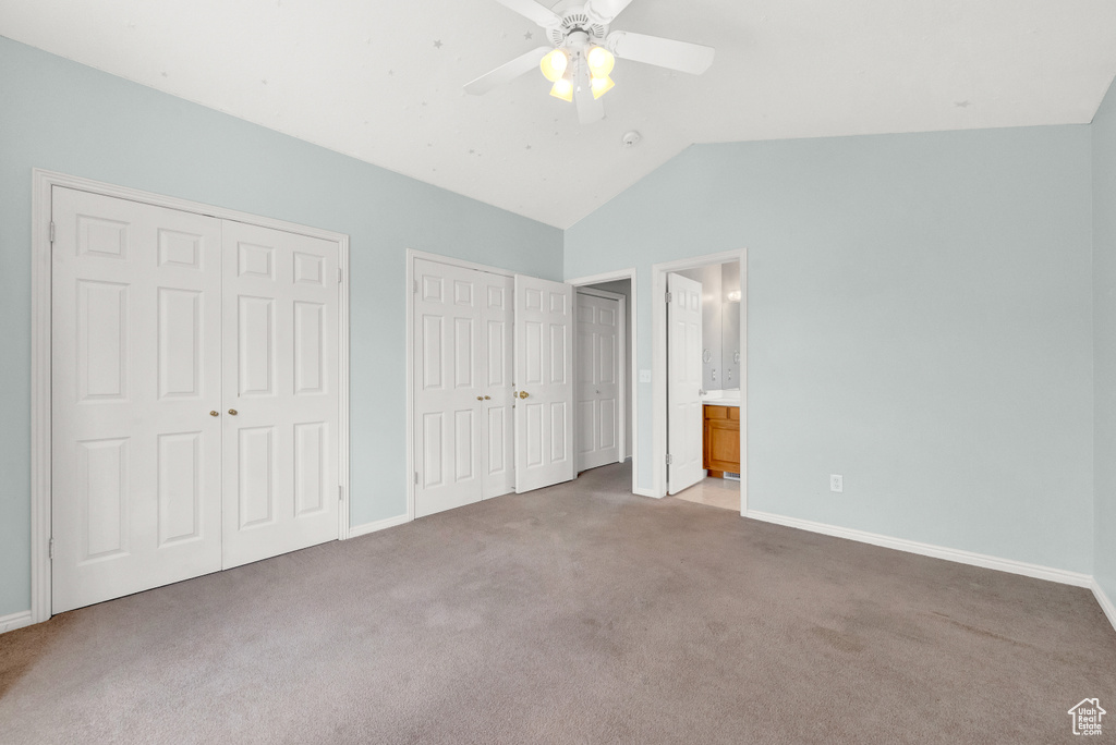 Unfurnished bedroom with ceiling fan, ensuite bathroom, dark colored carpet, and vaulted ceiling