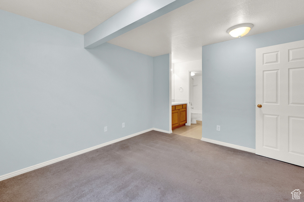 Unfurnished bedroom featuring beamed ceiling, light colored carpet, and ensuite bath