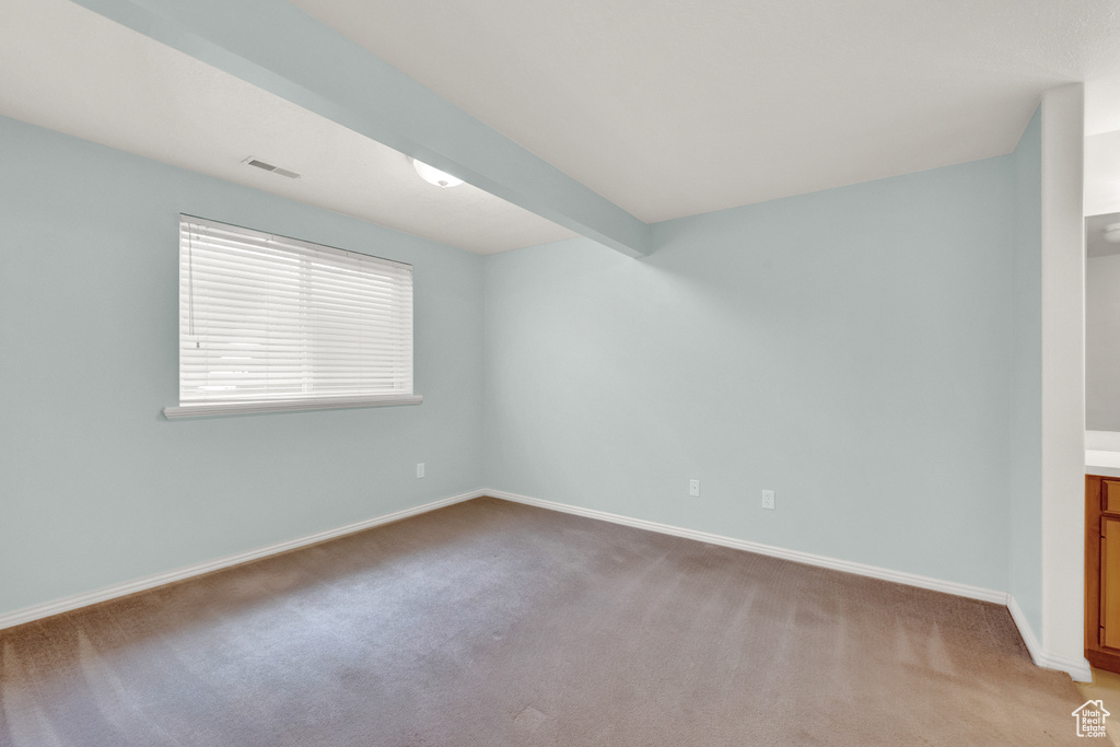 Spare room featuring beamed ceiling and light colored carpet