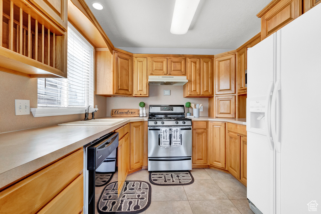 Kitchen featuring stainless steel range with gas stovetop, light tile flooring, white fridge with ice dispenser, dishwasher, and sink