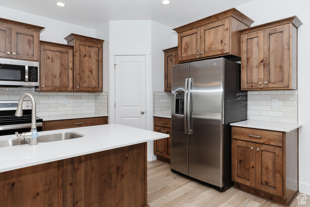 Kitchen featuring backsplash, stainless steel appliances, sink, and light wood-type flooring