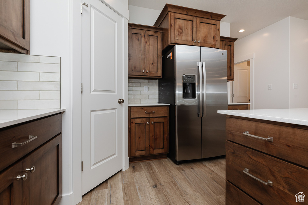 Kitchen featuring light hardwood / wood-style flooring, dark brown cabinets, tasteful backsplash, and stainless steel fridge with ice dispenser