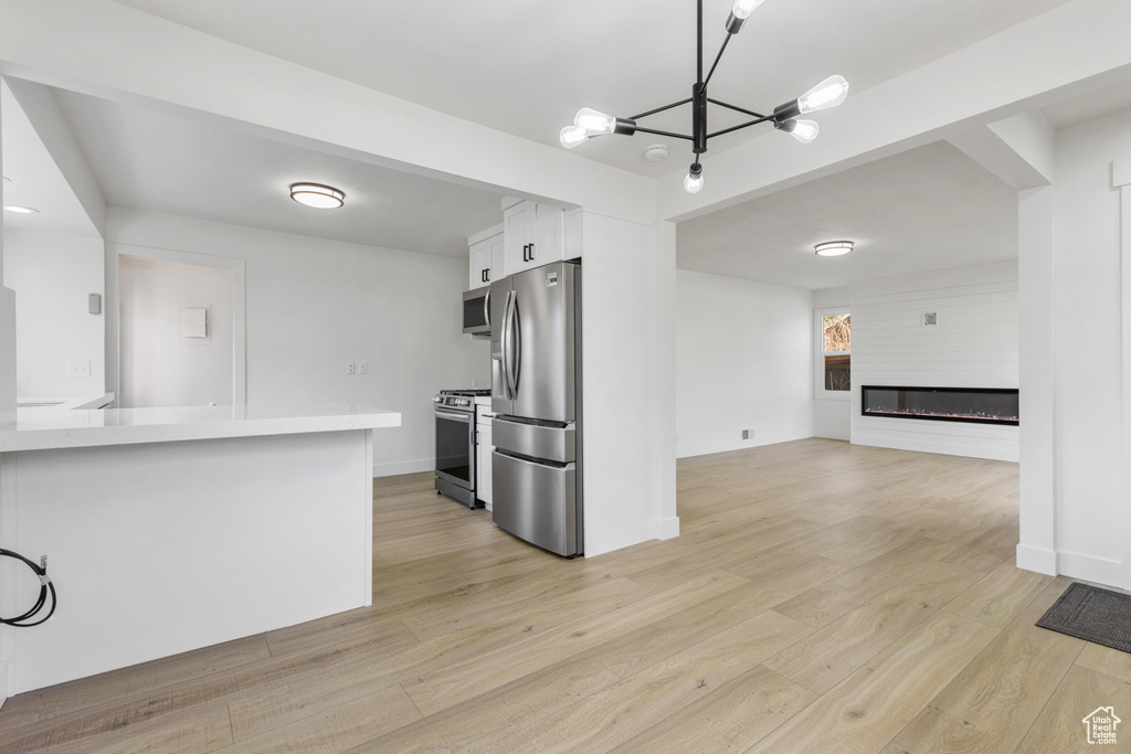 Kitchen with appliances with stainless steel finishes, light wood-type flooring, white cabinetry, and a chandelier