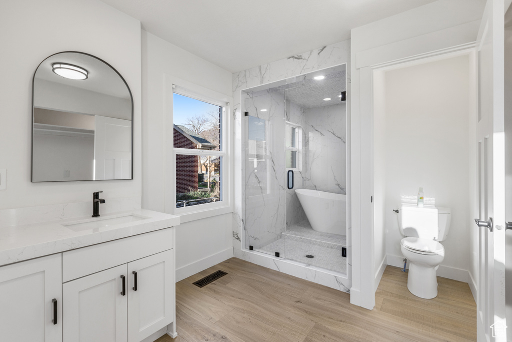 Bathroom featuring toilet, a shower with door, wood-type flooring, and vanity with extensive cabinet space