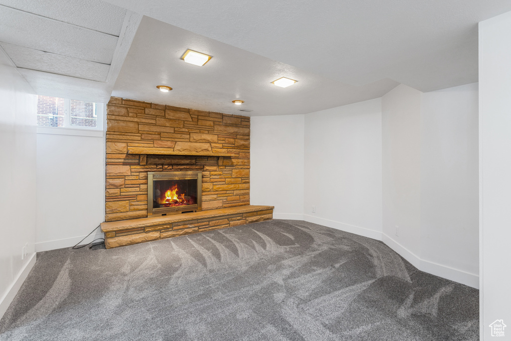 Unfurnished living room featuring a textured ceiling, carpet floors, and a stone fireplace