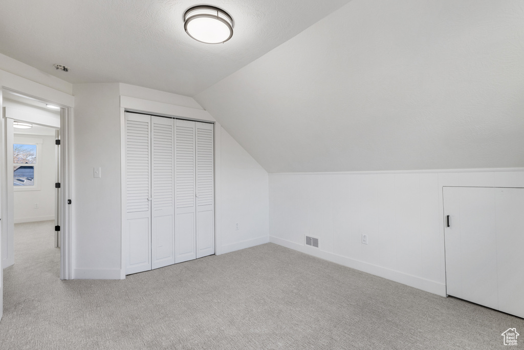 Additional living space with light carpet and vaulted ceiling