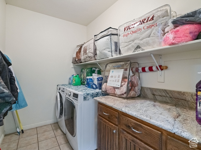 Washroom with light tile flooring, cabinets, and washing machine and clothes dryer