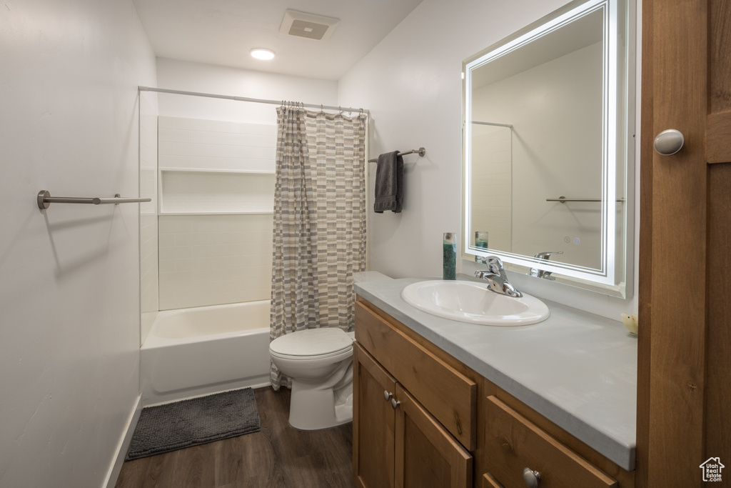 Full bathroom with large vanity, toilet, hardwood / wood-style floors, and shower / tub combo with curtain