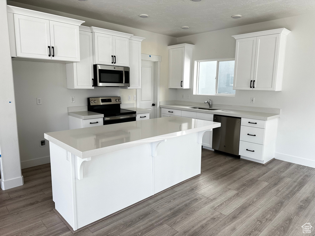 Kitchen with appliances with stainless steel finishes, a breakfast bar area, white cabinetry, and a center island