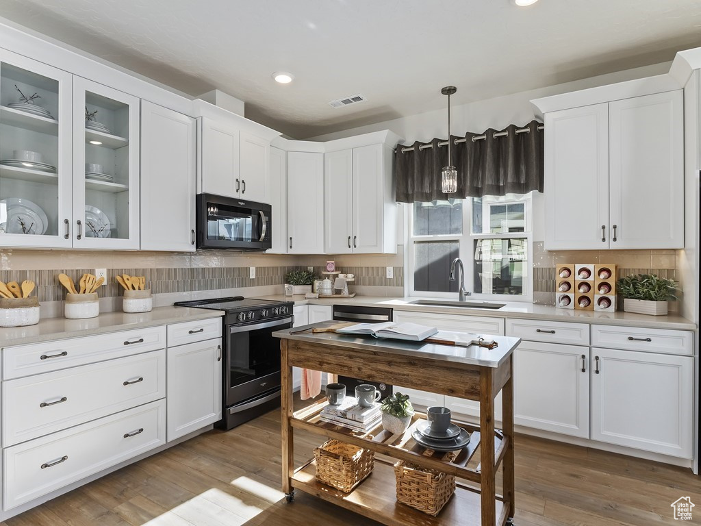 Kitchen with decorative light fixtures, tasteful backsplash, white cabinets, electric range, and sink
