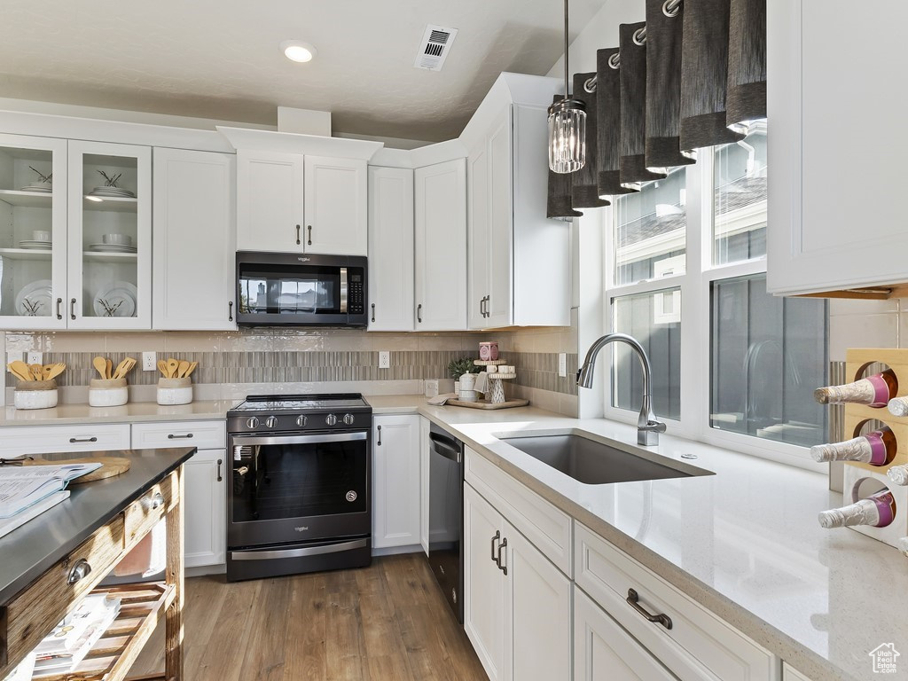 Kitchen with stainless steel appliances, decorative light fixtures, dark wood-type flooring, white cabinetry, and sink