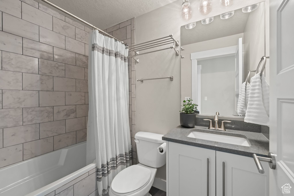 Full bathroom featuring shower / bath combo with shower curtain, toilet, vanity, and a textured ceiling
