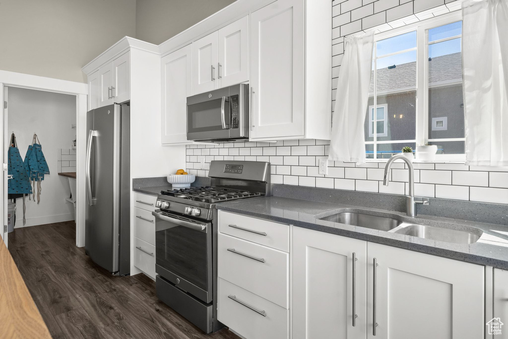 Kitchen with tasteful backsplash, dark wood-type flooring, stainless steel appliances, sink, and white cabinetry