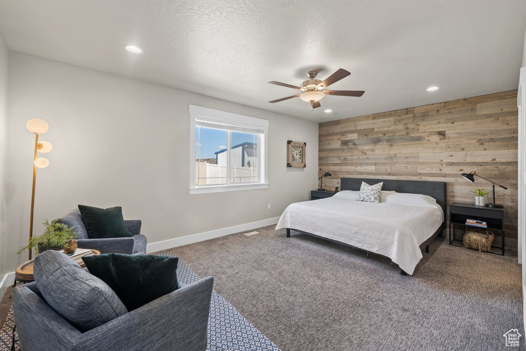 Bedroom featuring dark carpet, a textured ceiling, wood walls, and ceiling fan