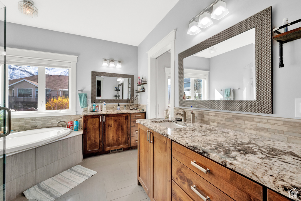 Bathroom with vanity with extensive cabinet space, tasteful backsplash, tile floors, and tiled tub