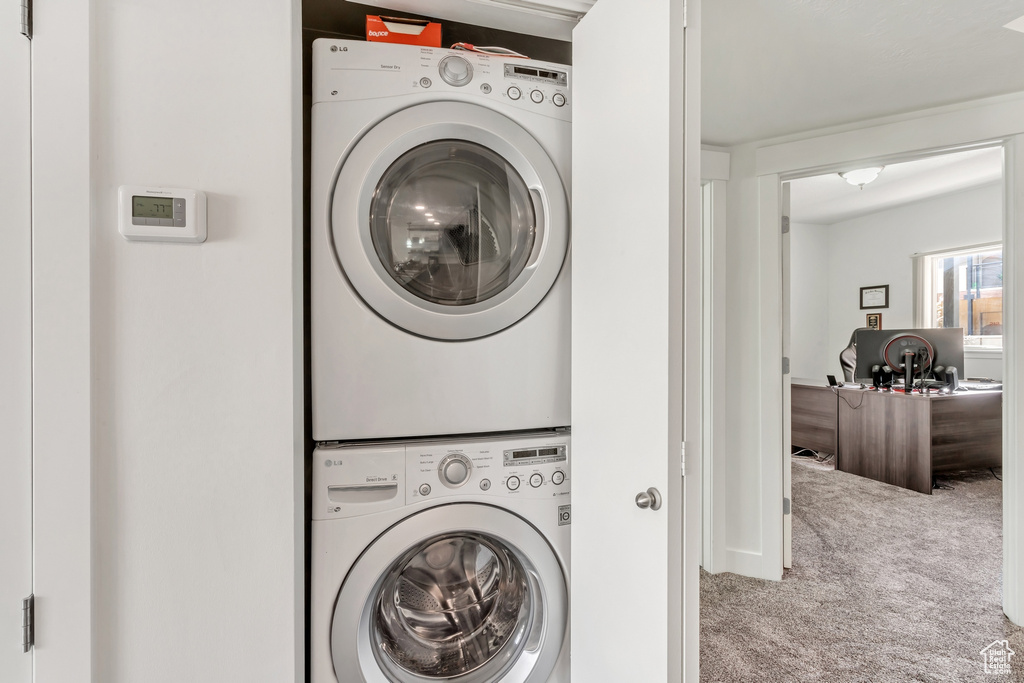 Laundry area featuring light colored carpet and stacked washer and dryer