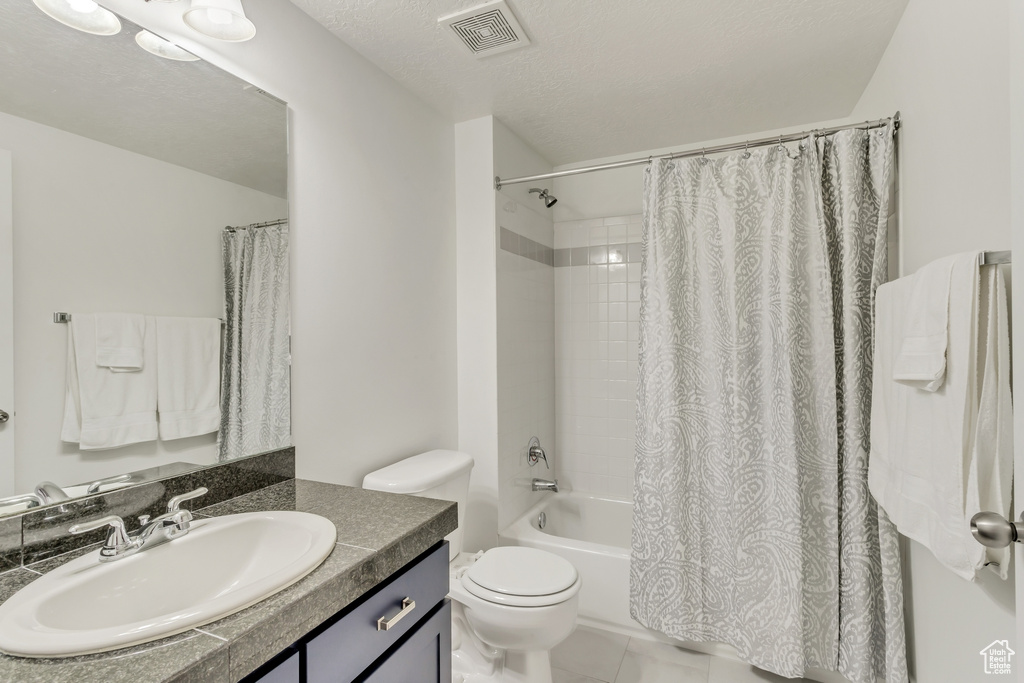 Full bathroom with shower / bath combo, toilet, tile floors, oversized vanity, and a textured ceiling