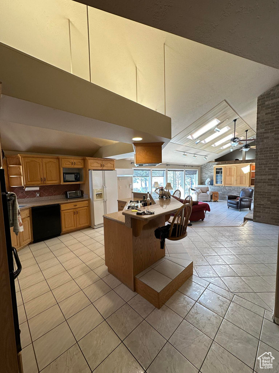 Kitchen featuring black appliances, ceiling fan, vaulted ceiling, and light tile floors