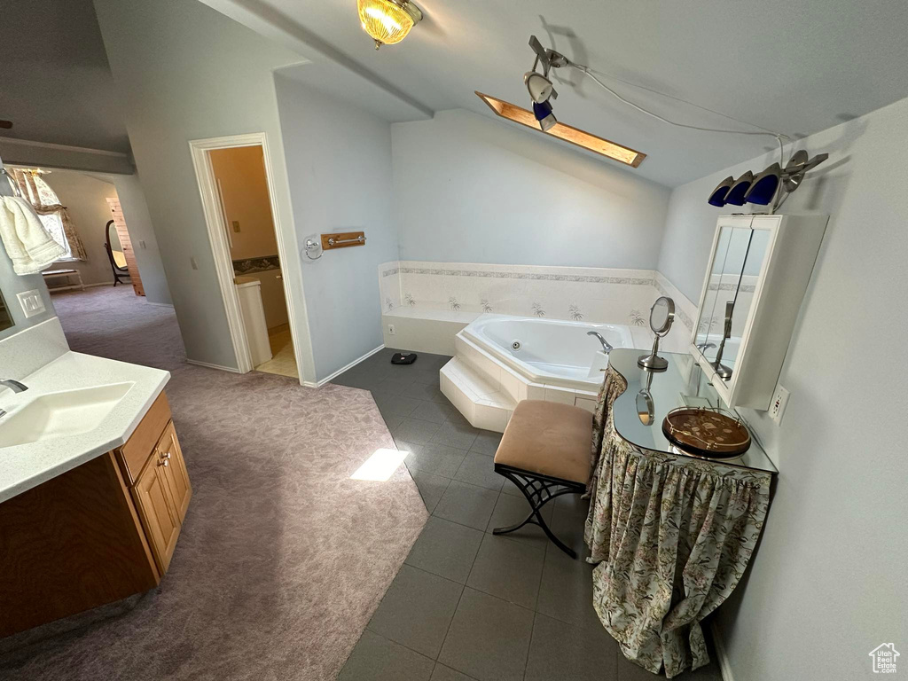 Bathroom with tiled bath, vaulted ceiling, tile floors, and vanity