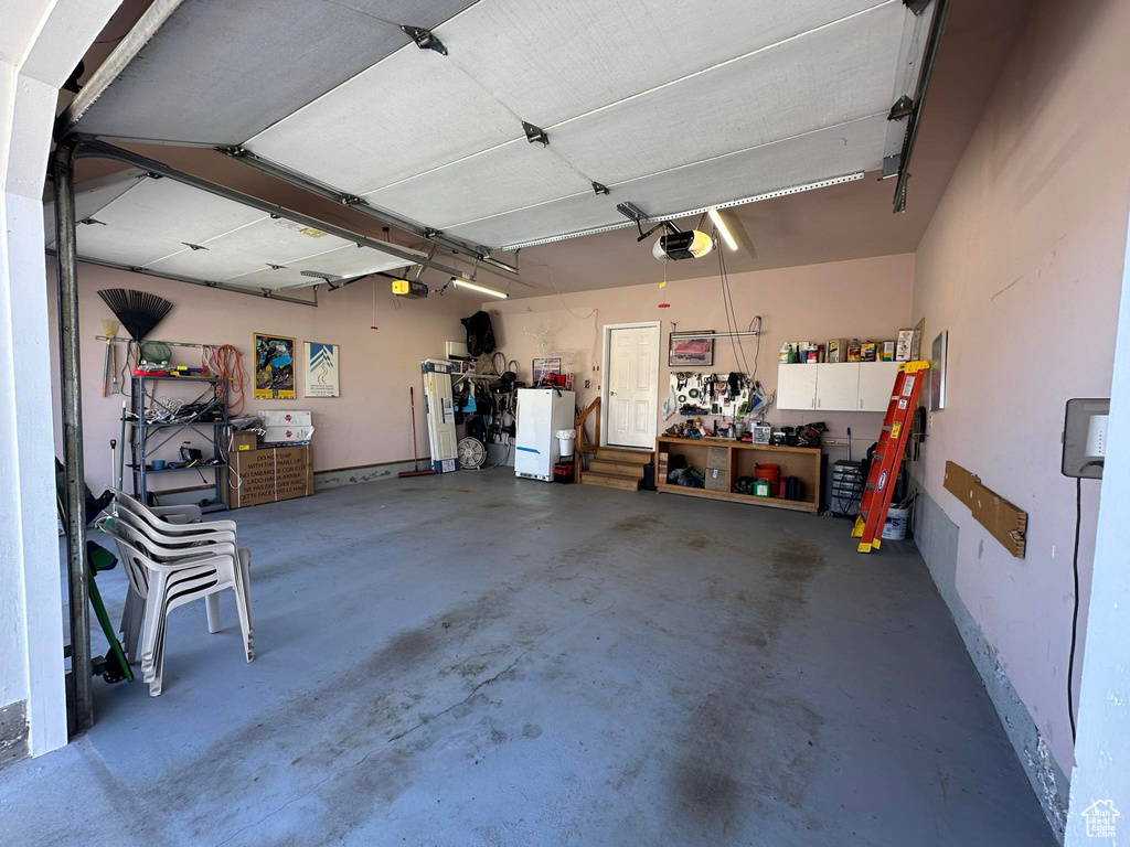 Garage featuring a garage door opener, white fridge, and a workshop area