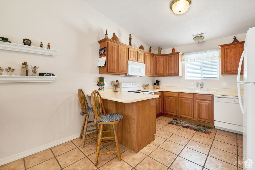 Kitchen with kitchen peninsula, white appliances, a kitchen breakfast bar, sink, and light tile floors