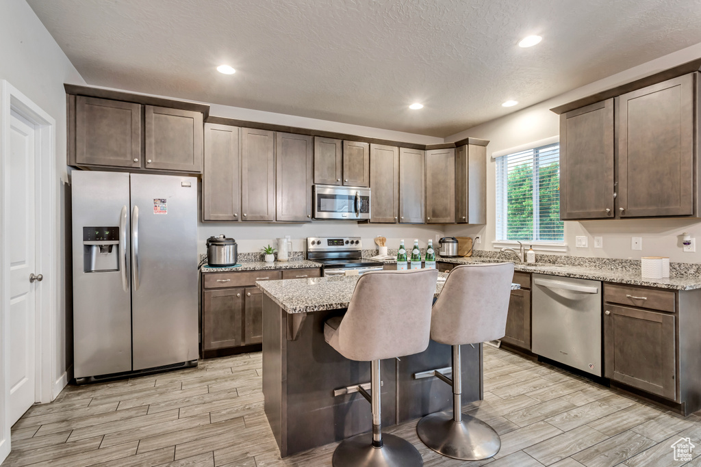 Kitchen featuring appliances with stainless steel finishes, light stone countertops, a center island, and a breakfast bar