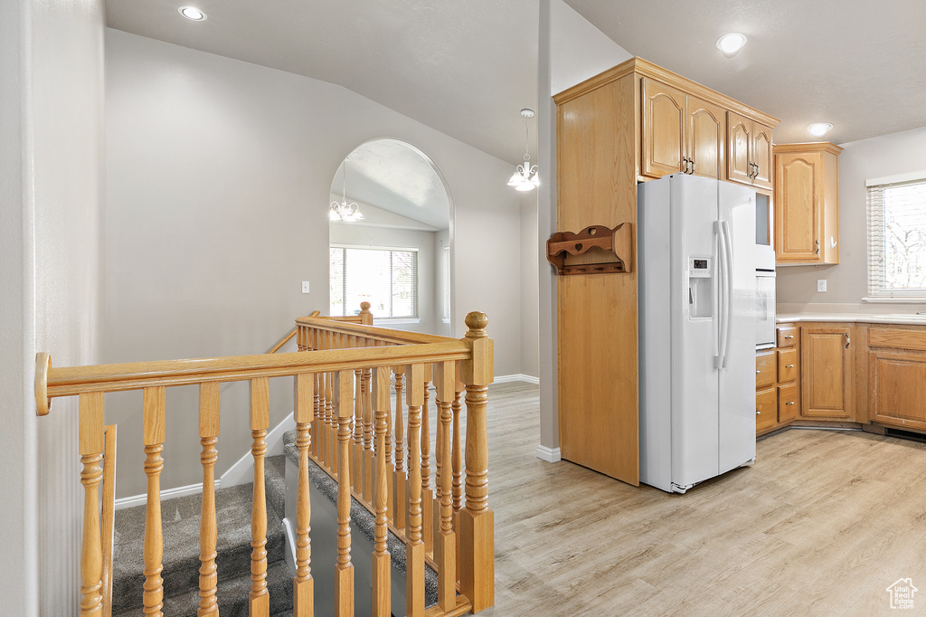 Kitchen featuring white refrigerator with ice dispenser, lofted ceiling, a wealth of natural light, and light wood-type flooring