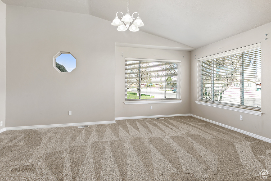Spare room with light colored carpet, vaulted ceiling, and a notable chandelier