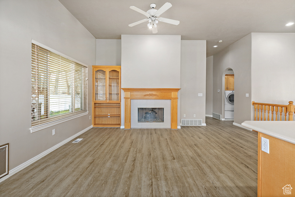 Unfurnished living room with light hardwood / wood-style floors, a high ceiling, ceiling fan, washer / clothes dryer, and a tiled fireplace
