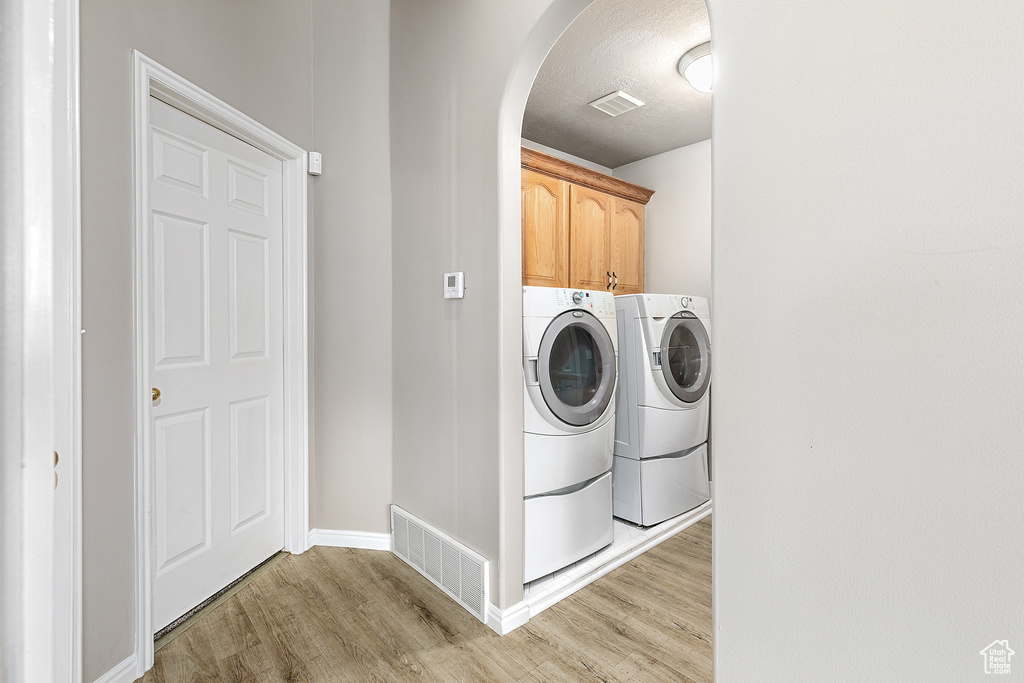 Laundry area with washing machine and clothes dryer, light hardwood / wood-style flooring, and cabinets