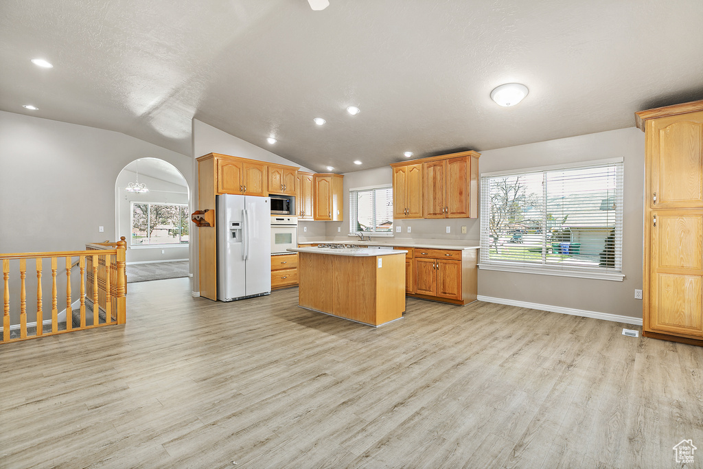 Kitchen featuring white appliances, a kitchen island, light hardwood / wood-style floors, and vaulted ceiling