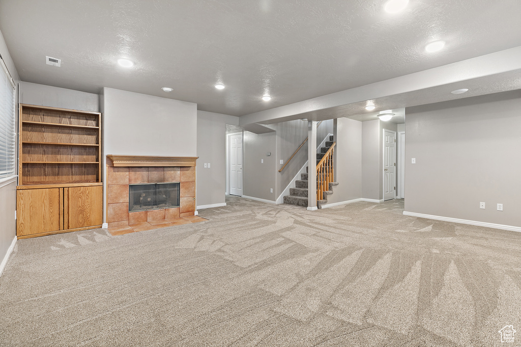 Unfurnished living room featuring built in features, light colored carpet, a fireplace, and a textured ceiling