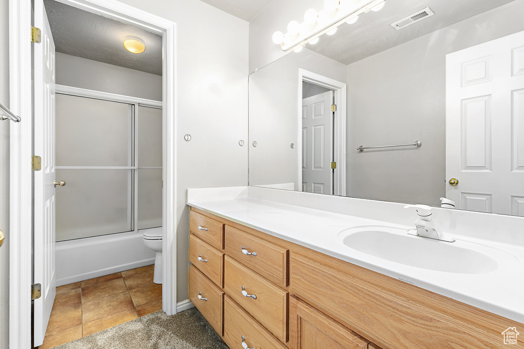 Full bathroom with toilet, vanity with extensive cabinet space, tile flooring, and bath / shower combo with glass door