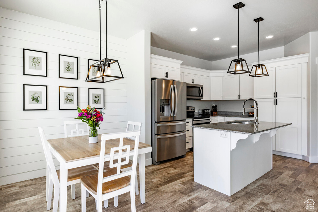 Kitchen with hanging light fixtures, stainless steel appliances, dark wood-type flooring, and a kitchen island with sink