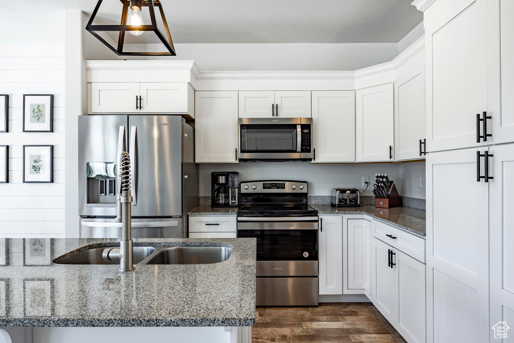 Kitchen featuring appliances with stainless steel finishes, white cabinetry, dark stone counters, dark wood-type flooring, and hanging light fixtures