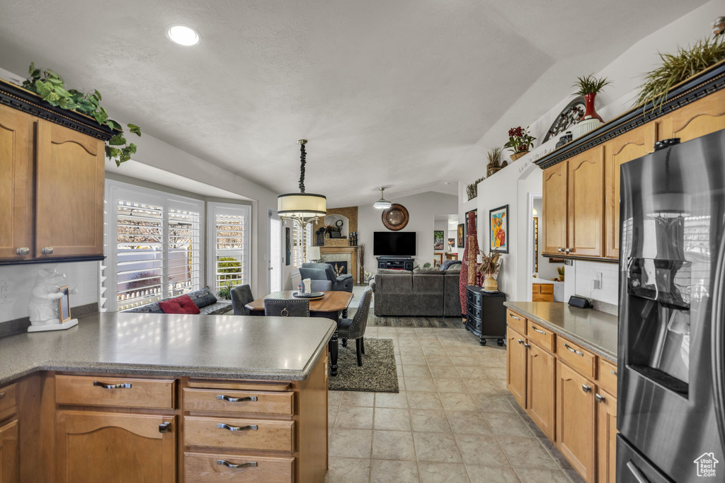 Kitchen featuring light tile floors, lofted ceiling, decorative light fixtures, and black fridge