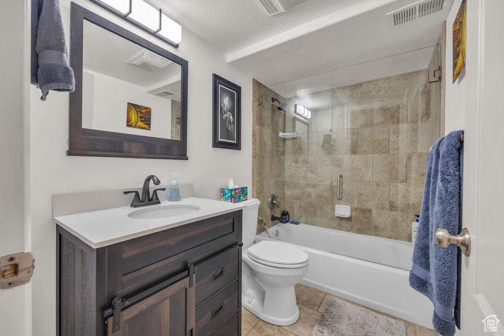 Full bathroom featuring tiled shower / bath combo, toilet, tile floors, oversized vanity, and a textured ceiling