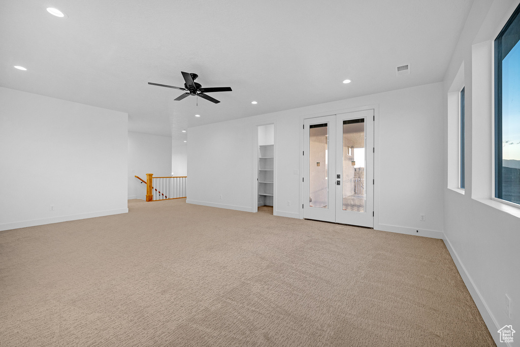 Carpeted spare room featuring ceiling fan, french doors, and plenty of natural light