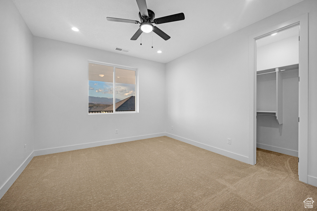 Unfurnished bedroom featuring light carpet, a walk in closet, a closet, and ceiling fan